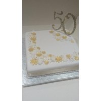 A square cake beautifully decorated with sugar flowers and a sparkly 50